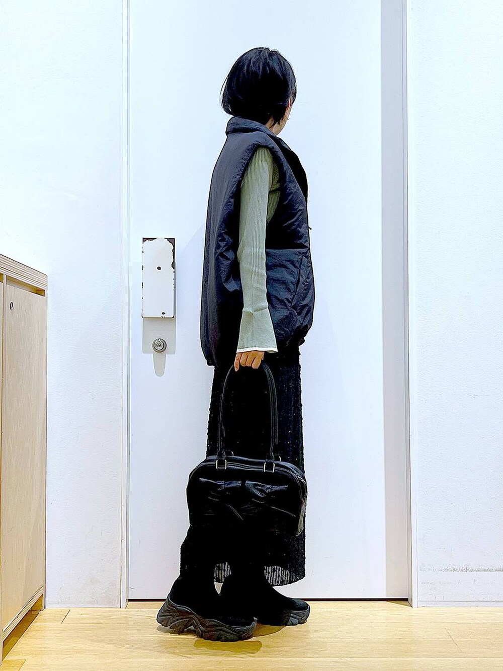 グリーン系のニット/セーター、ブラック系のハンドバッグ、ブラック系のブーツを着用したレディースの秋コーディネートの4枚目の写真