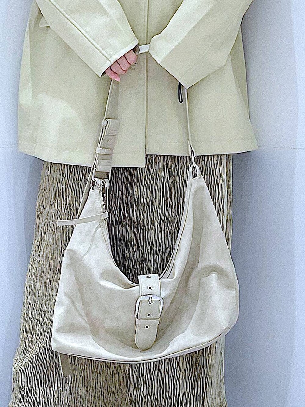 ベージュ系のステンカラーコート、ブラック系のブーツ、ホワイト系のショルダーバッグを着用したレディースの冬コーディネートの9枚目の写真