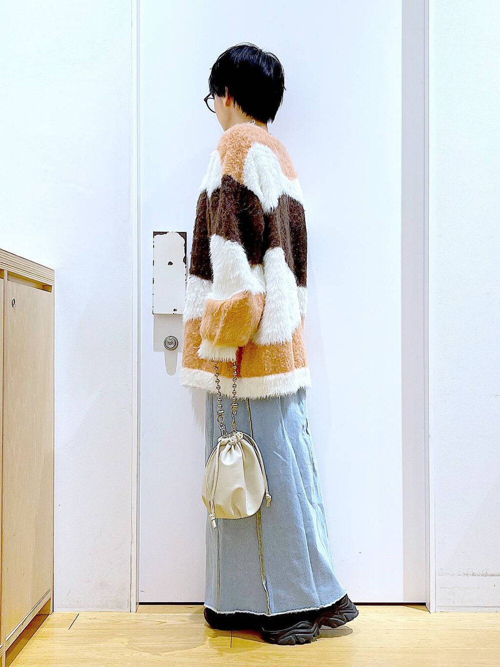 ベージュ系のショルダーバッグ、ブルー系のデニムスカート、ブラック系のブーツを着用したレディースの冬コーディネートの3枚目の写真