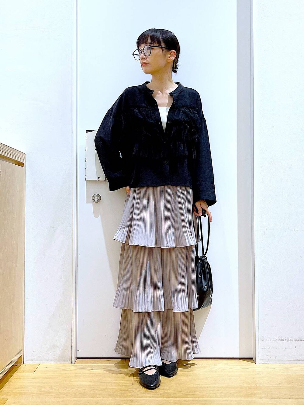 グレー系のスカート、ブラック系のショルダーバッグ、ブラック系のパンプスを着用したレディースの秋コーディネートの2枚目の写真