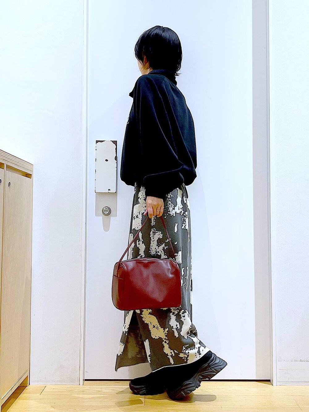 グレー系のスカート、レッド系のショルダーバッグ、ブラック系のブーツを着用したレディースの冬コーディネートの3枚目の写真