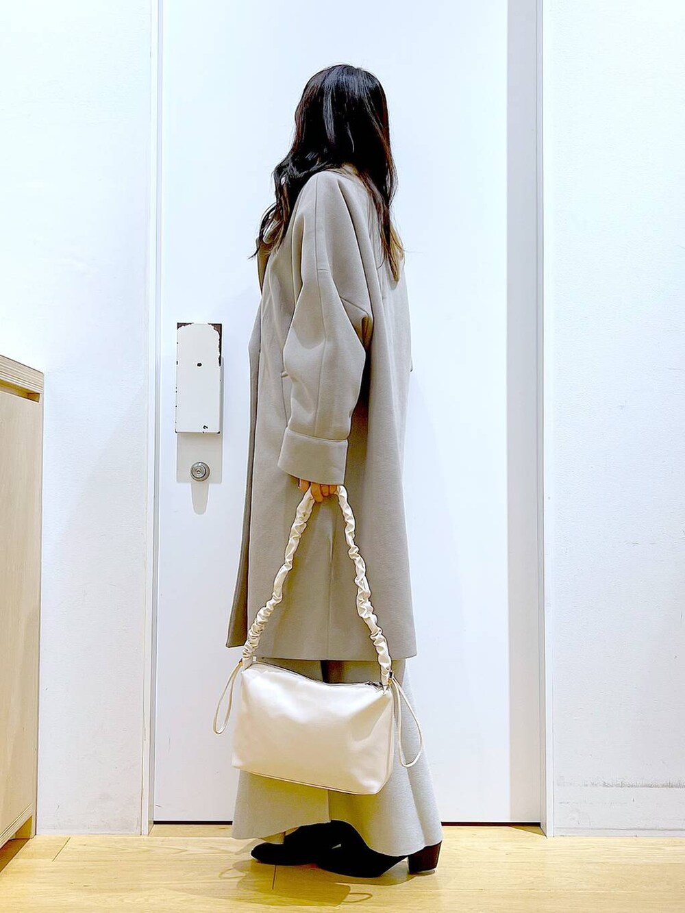 グレー系のステンカラーコート、ホワイト系のショルダーバッグ、グレー系のスカートを着用したレディースの冬コーディネートの3枚目の写真