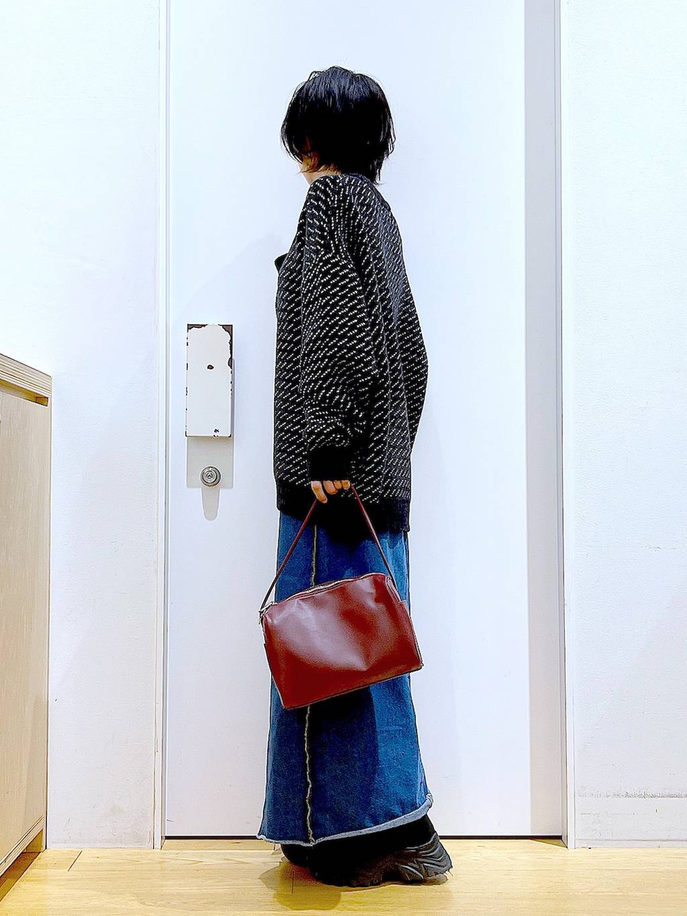 レッド系のショルダーバッグ、ブルー系のデニムスカート、ブラック系のニット/セーターを着用したレディースの冬コーディネートの3枚目の写真