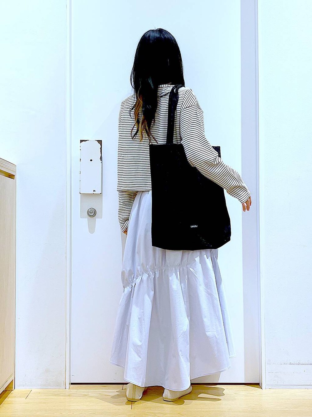 ブラック系のトートバッグ、ブルー系のスカート、イエロー系のニット/セーターを着用したレディースの春コーディネートの5枚目の写真