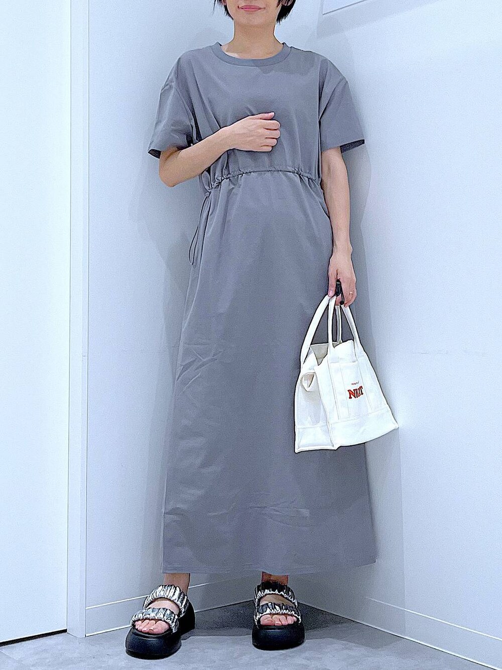 シルバー系のサンダル、グレー系のワンピース、ホワイト系のトートバッグを着用したレディースの夏コーディネートの6枚目の写真