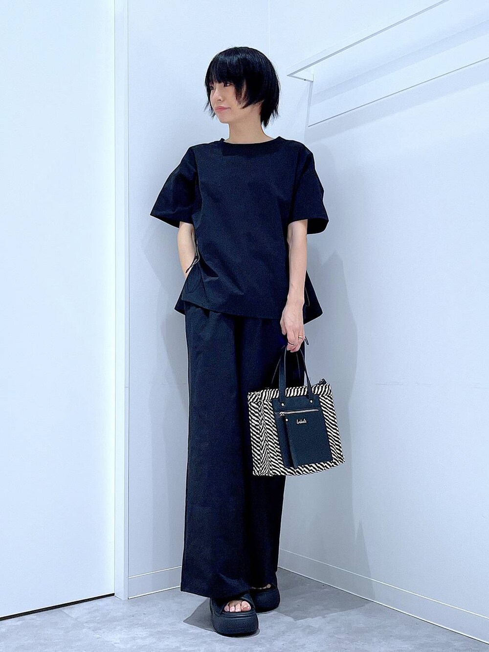 ブラック系のショルダーバッグ、ブラック系のサンダル、ブラック系のTシャツ/カットソーを着用したレディースの夏コーディネートの2枚目の写真