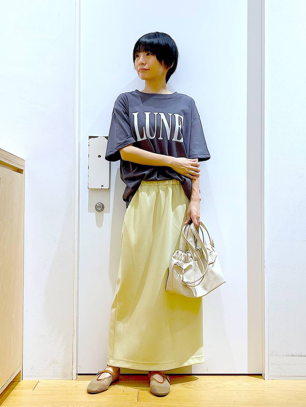 ホワイト系のショルダーバッグ、ベージュ系のパンプス、イエロー系のスカートを着用したレディースの夏コーディネートの2枚目の写真