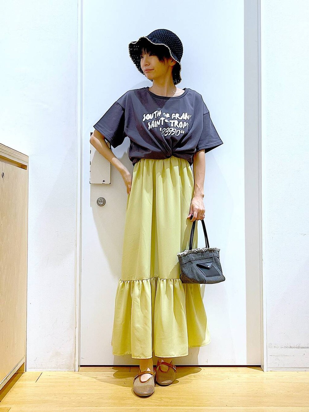 ブラック系のショルダーバッグ、ベージュ系のパンプス、イエロー系のワンピースを着用したレディースの春コーディネートの2枚目の写真