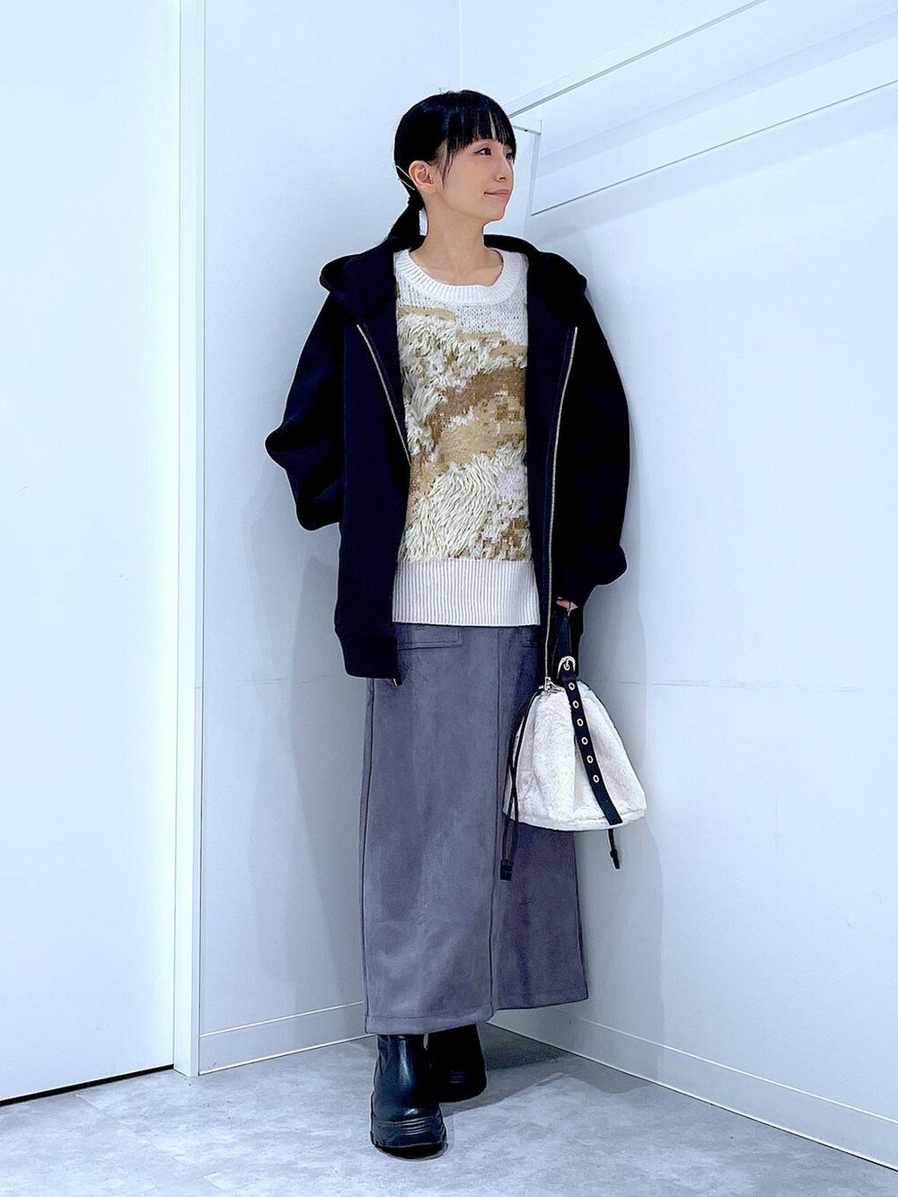 ホワイト系のハンドバッグ、ブラック系のブーツ、グレー系のスカートを着用したレディースの冬コーディネートの2枚目の写真