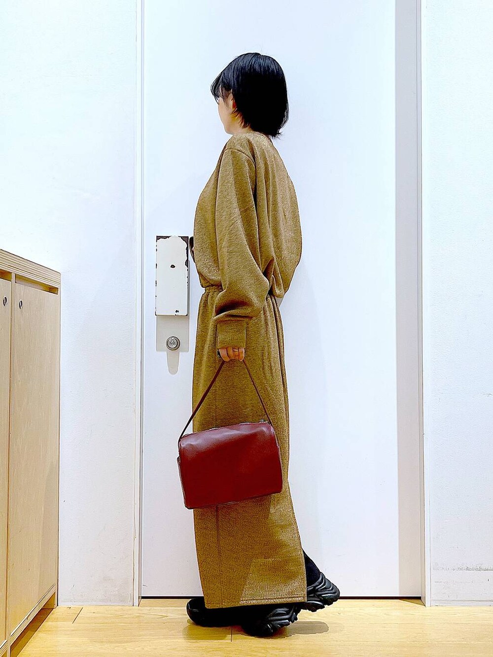 レッド系のショルダーバッグ、ブラック系のブーツ、ブラウン系のスウェットを着用したレディースの冬コーディネートの3枚目の写真