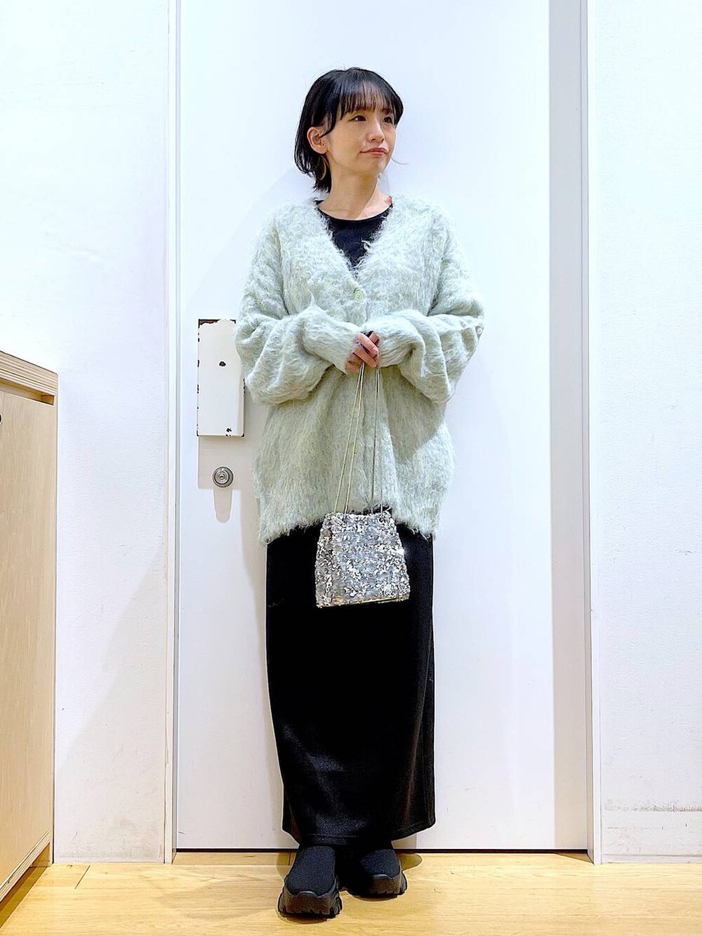 グリーン系のカーディガン/ボレロ、ブラック系のブーツ、ブラック系のスカートを着用したレディースの冬コーディネートの2枚目の写真