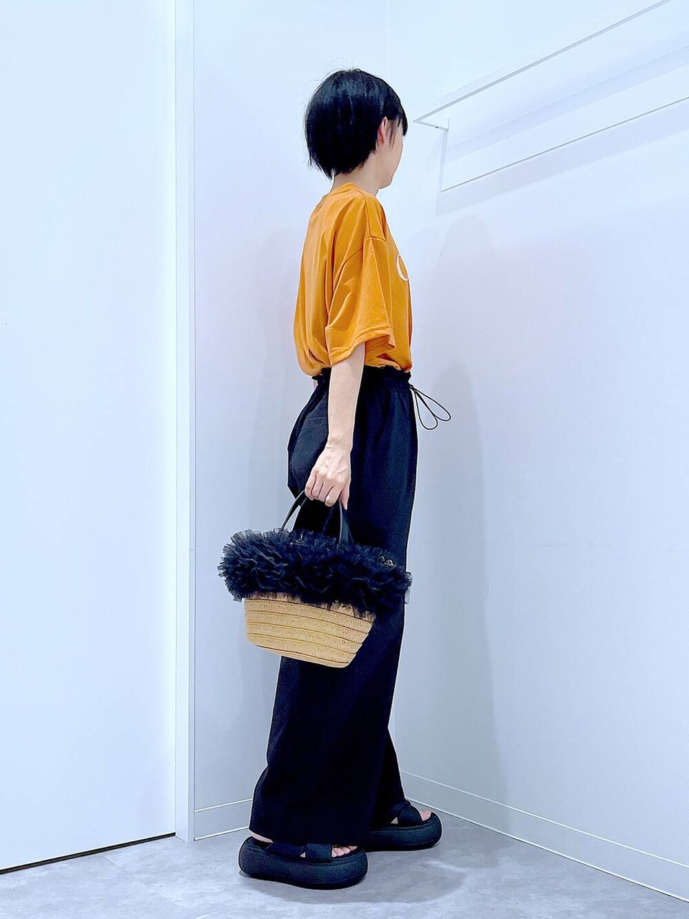 ベージュ系のショルダーバッグ、ブラック系のサンダル、オレンジ系のTシャツ/カットソーを着用したレディースの夏コーディネートの4枚目の写真