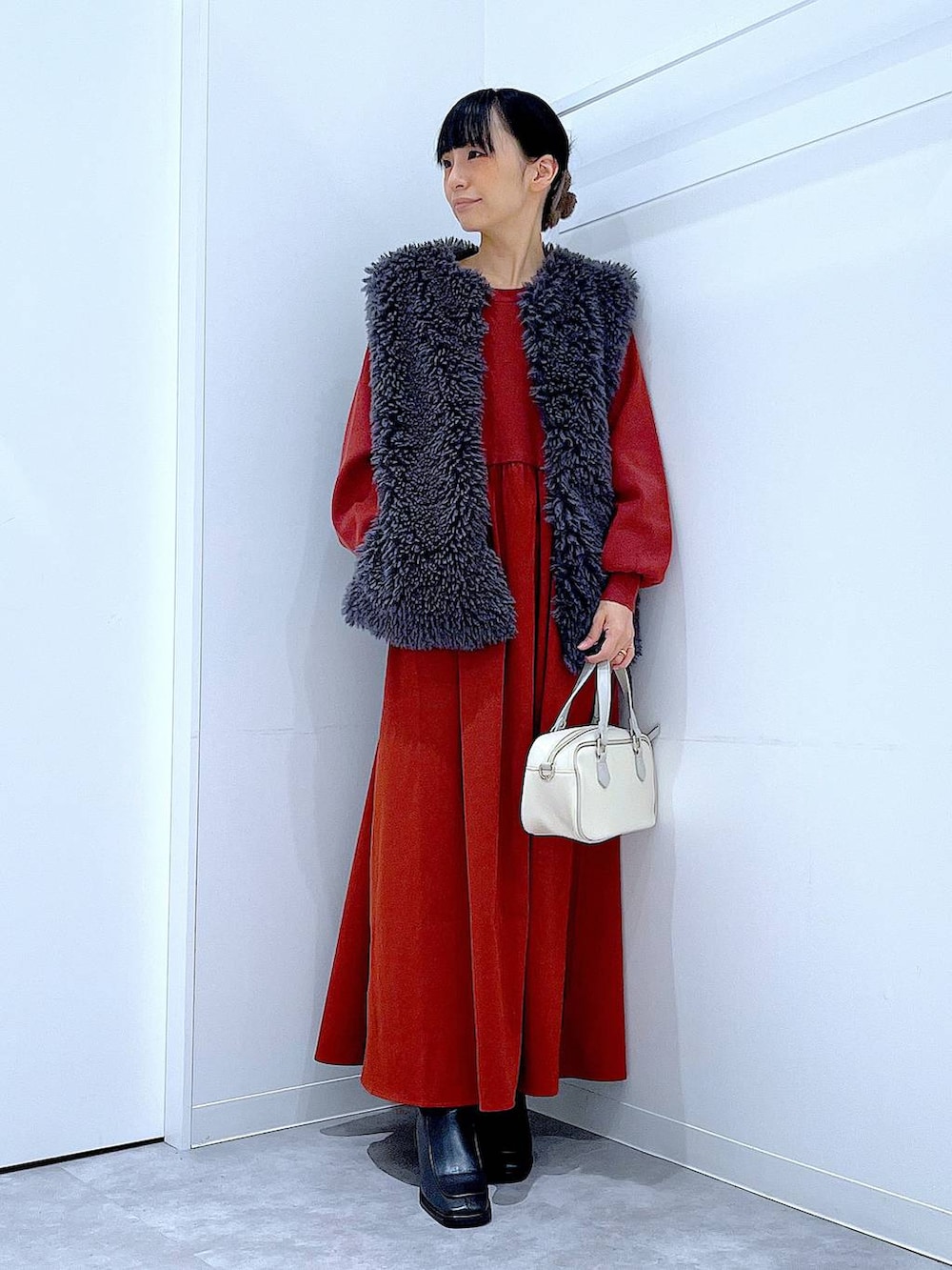 グレー系のベスト、ブラック系のブーツ、ホワイト系のショルダーバッグを着用したレディースの秋コーディネートの2枚目の写真