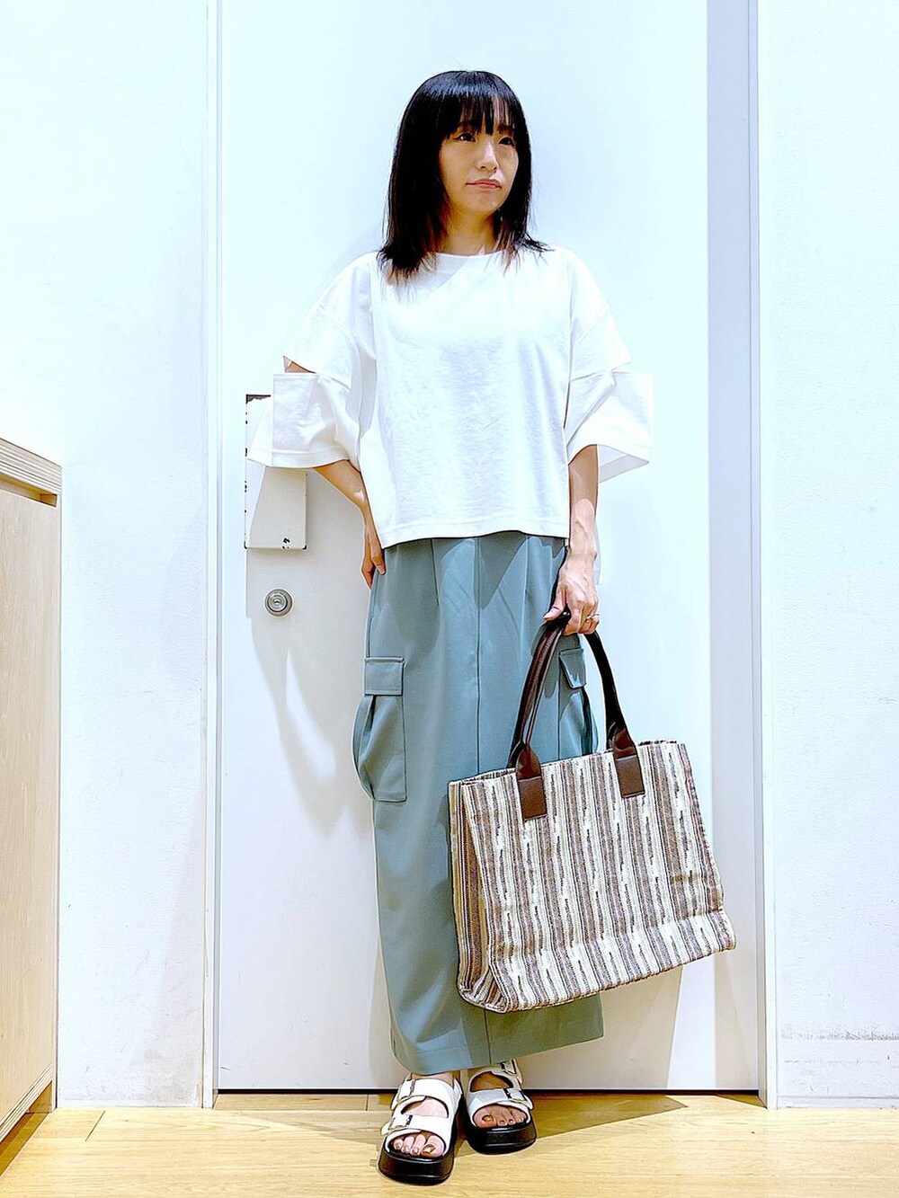ホワイト系のサンダル、グリーン系のスカート、ブラウン系のトートバッグを着用したレディースの夏コーディネートの2枚目の写真