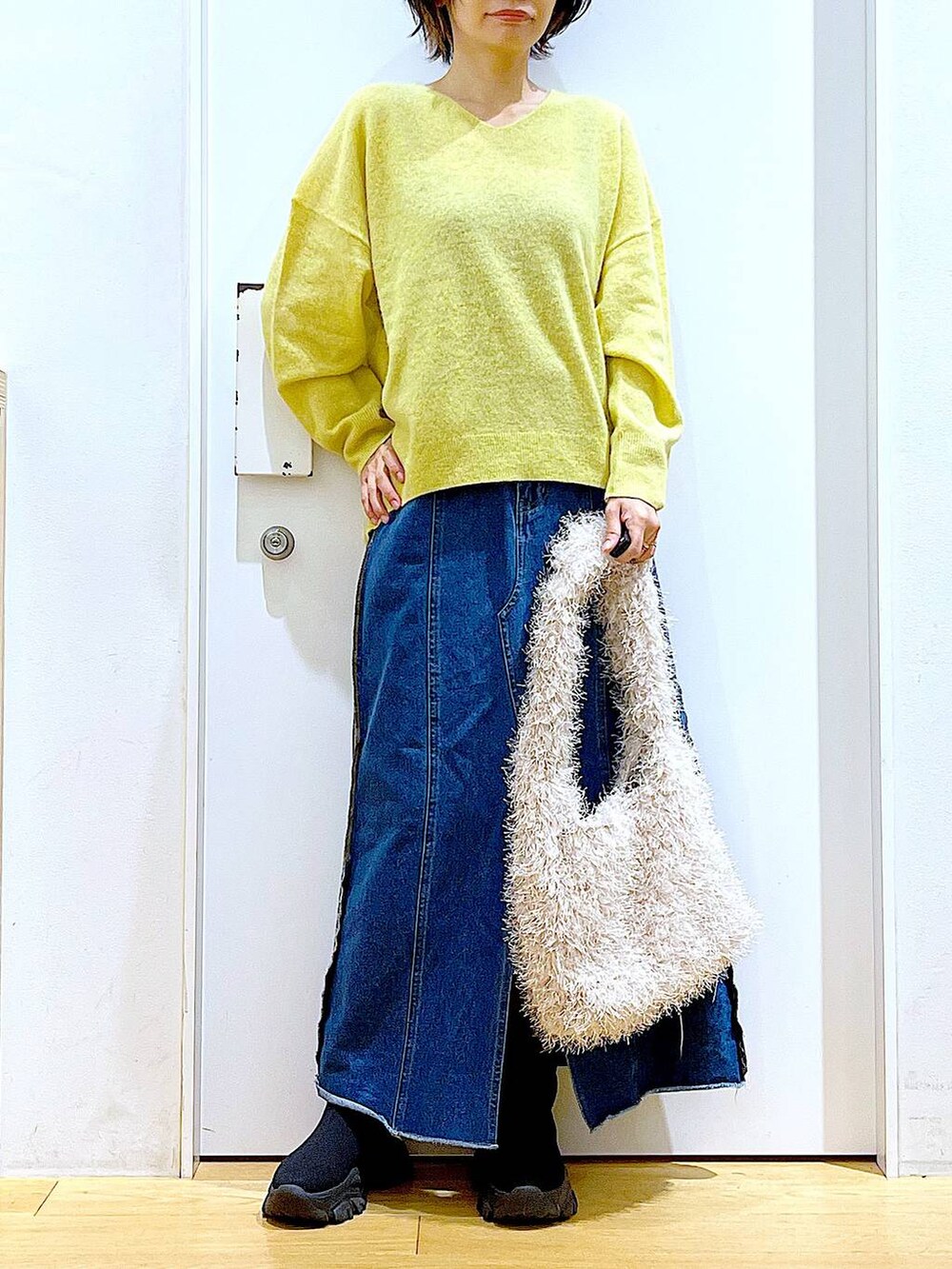 イエロー系のニット/セーター、ブルー系のデニムスカート、ベージュ系のショルダーバッグを着用したレディースの冬コーディネートの6枚目の写真