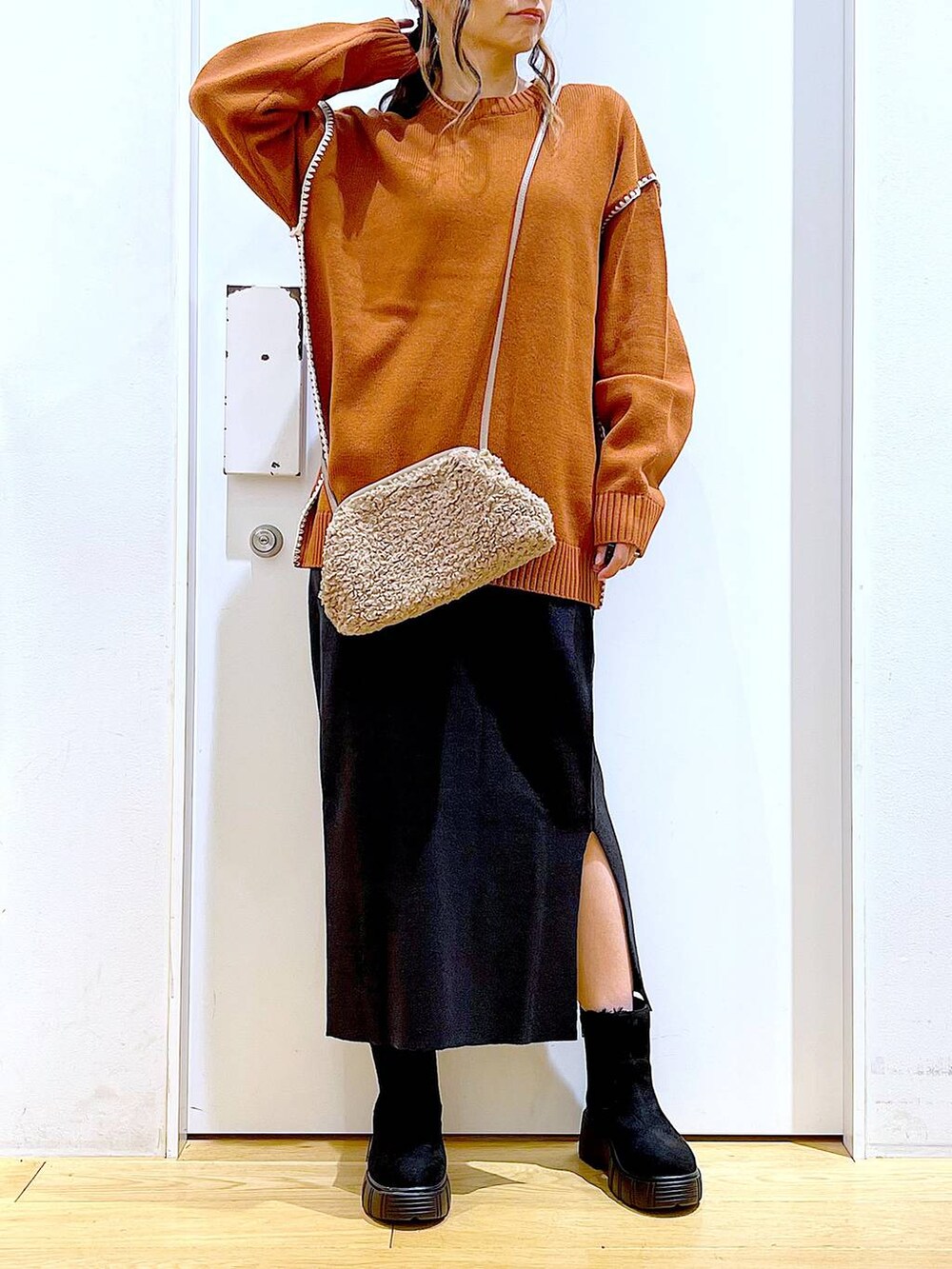 グレー系のスカート、オレンジ系のニット/セーター、ブラウン系のクラッチバッグを着用したレディースの冬コーディネートの6枚目の写真
