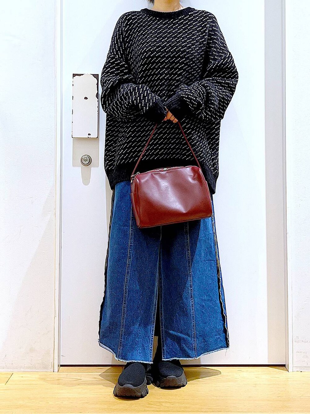 レッド系のショルダーバッグ、ブルー系のデニムスカート、ブラック系のニット/セーターを着用したレディースの冬コーディネートの6枚目の写真