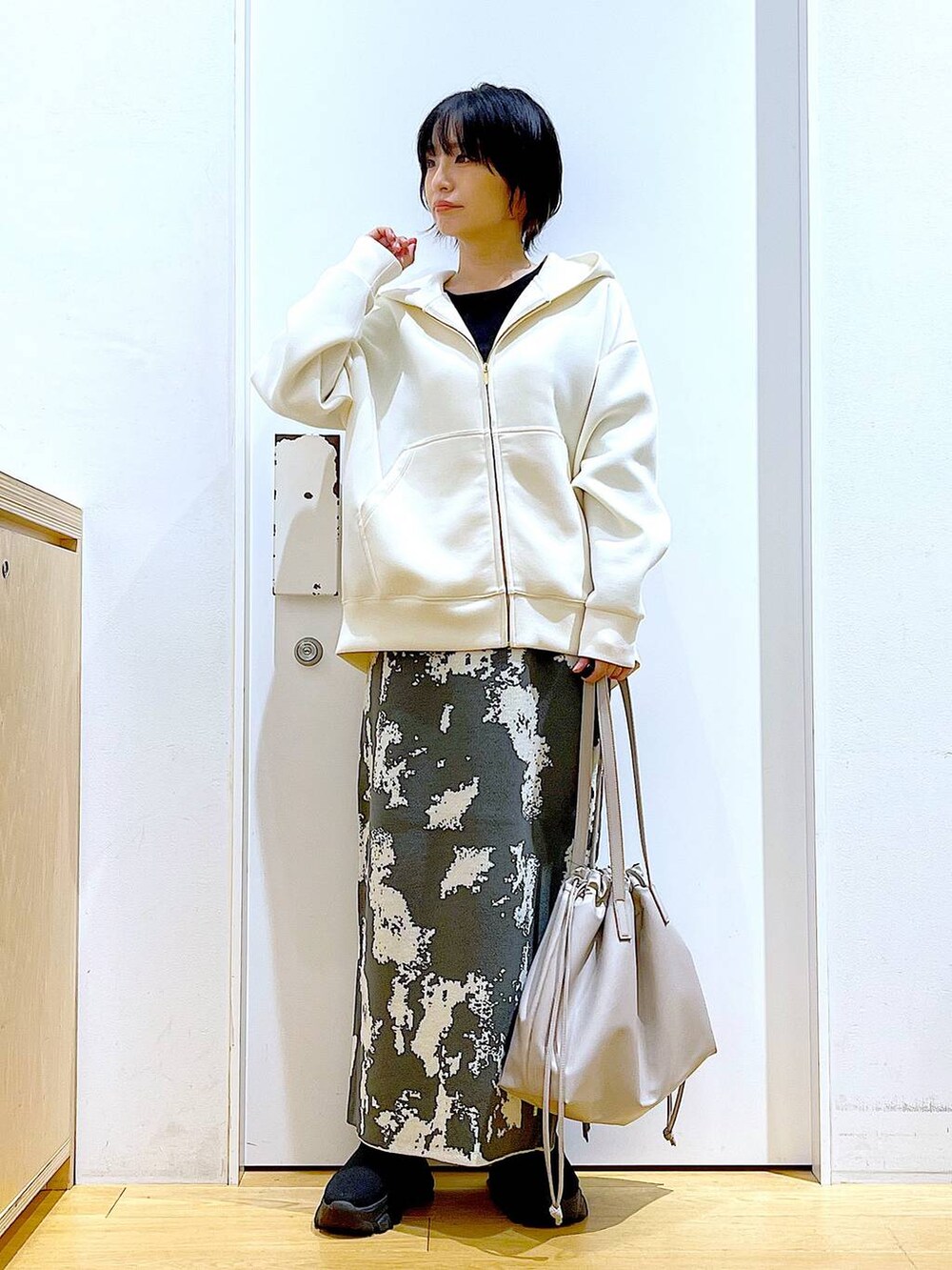 グレー系のスカート、ベージュ系のトートバッグ、ブラック系のブーツを着用したレディースの秋コーディネートの2枚目の写真