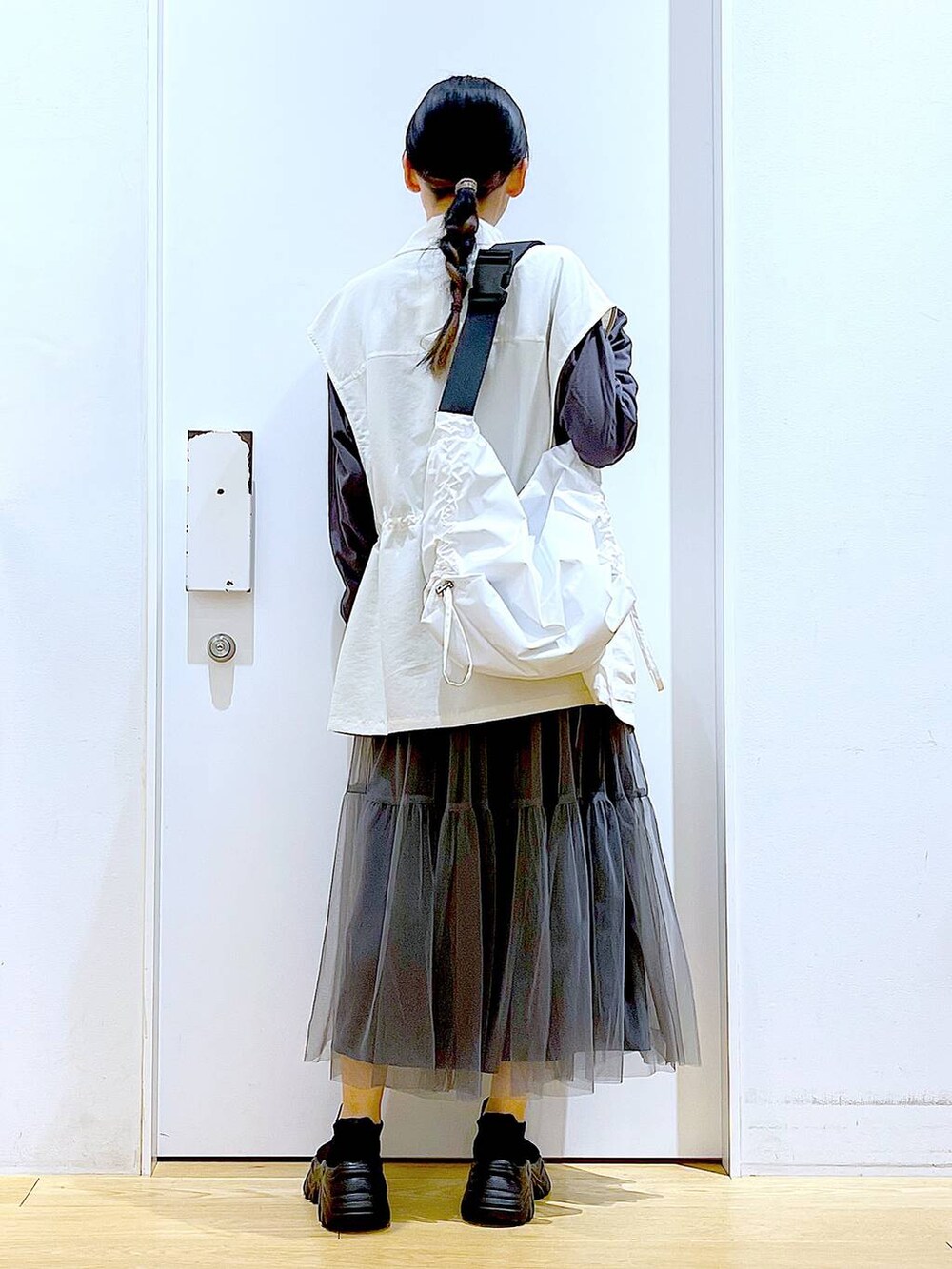 グレー系のスカート、ブラック系のスニーカー、ホワイト系のベストを着用したレディースの春コーディネートの5枚目の写真