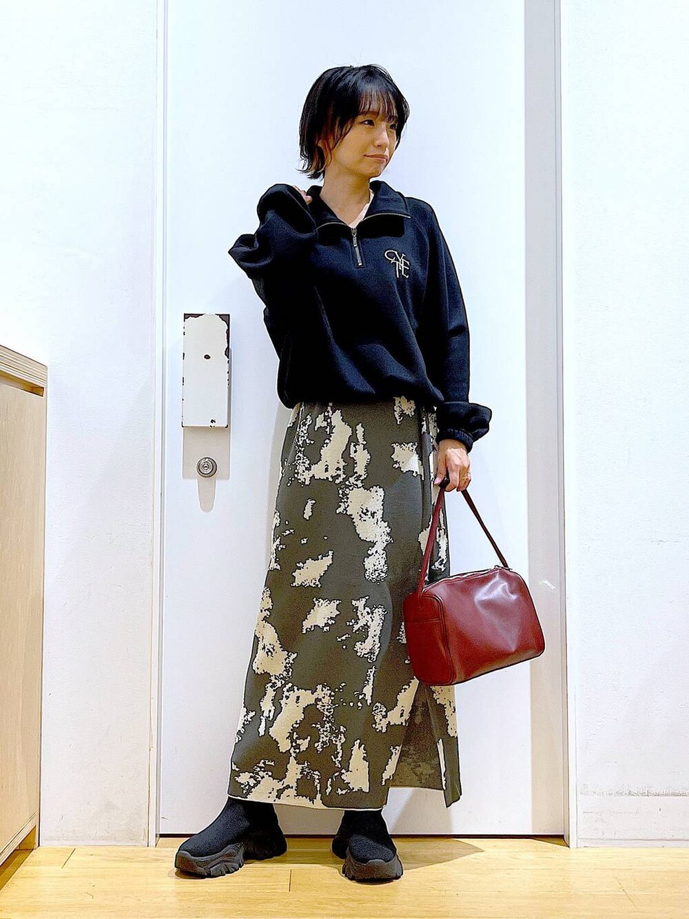 グレー系のスカート、レッド系のショルダーバッグ、ブラック系のブーツを着用したレディースの冬コーディネートの2枚目の写真