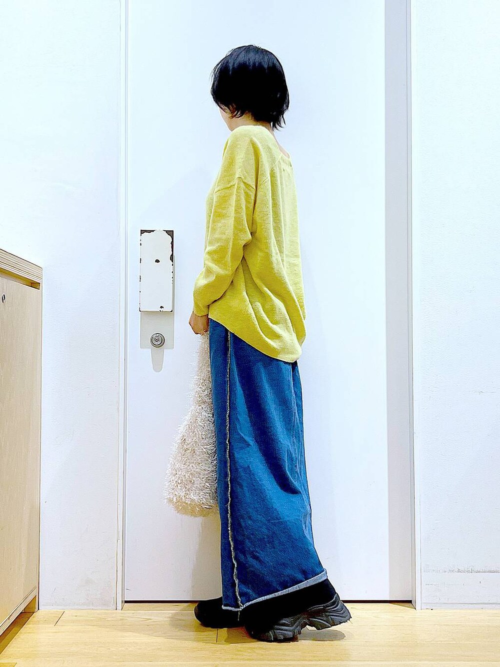 イエロー系のニット/セーター、ブルー系のデニムスカート、ベージュ系のショルダーバッグを着用したレディースの冬コーディネートの3枚目の写真