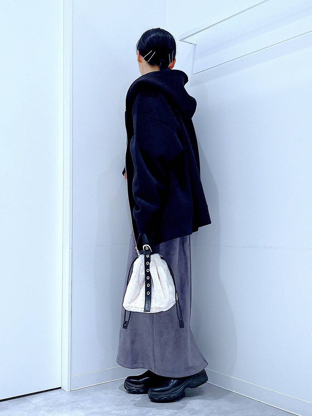 ホワイト系のハンドバッグ、ブラック系のブーツ、グレー系のスカートを着用したレディースの冬コーディネートの3枚目の写真