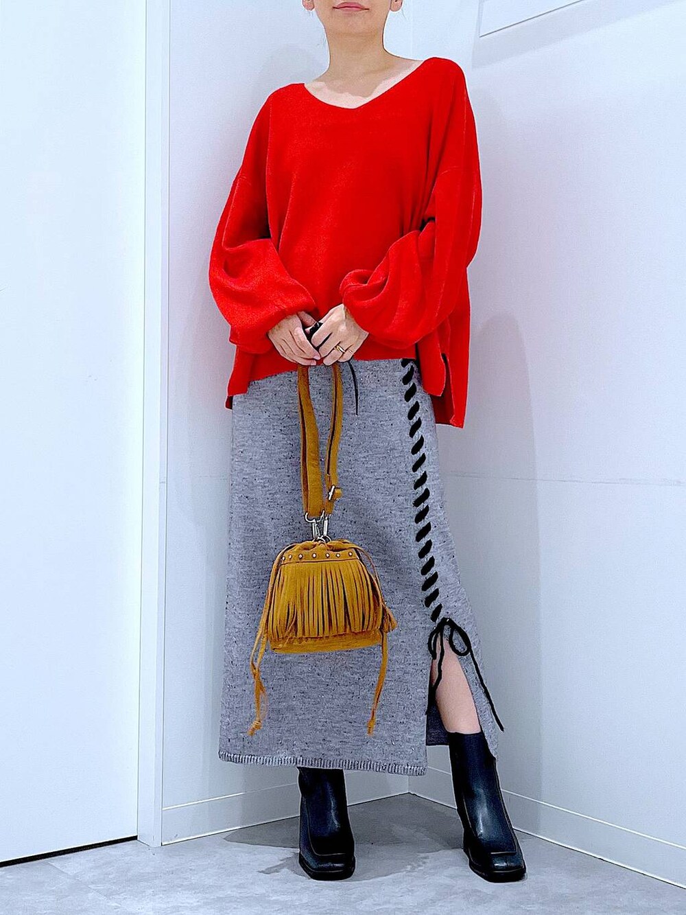 レッド系のニット/セーター、グレー系のスカート、ブラック系のブーツを着用したレディースの秋コーディネートの6枚目の写真