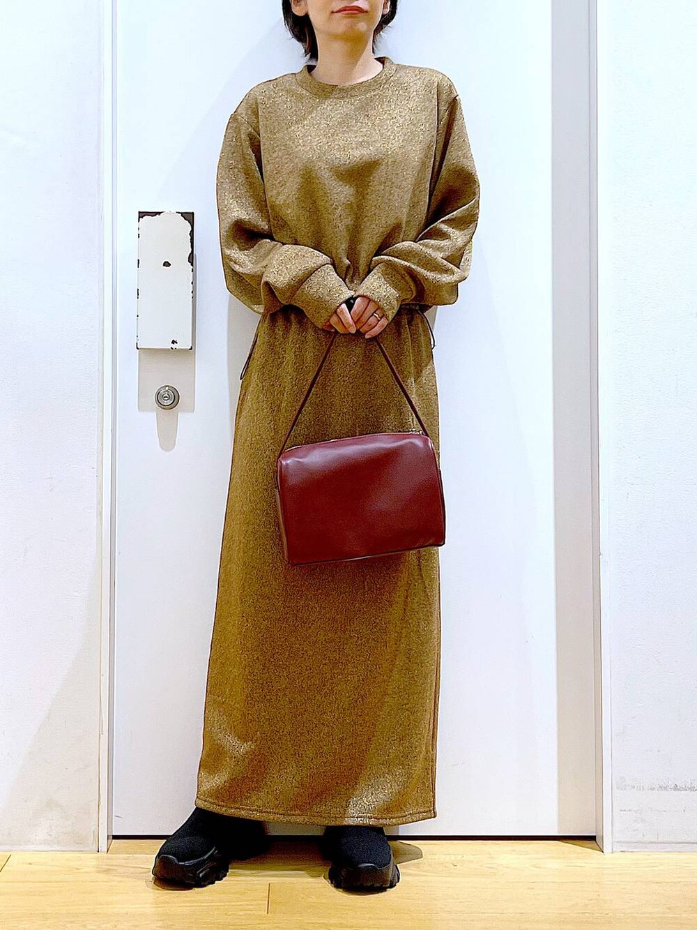 レッド系のショルダーバッグ、ブラック系のブーツ、ブラウン系のスウェットを着用したレディースの冬コーディネートの6枚目の写真