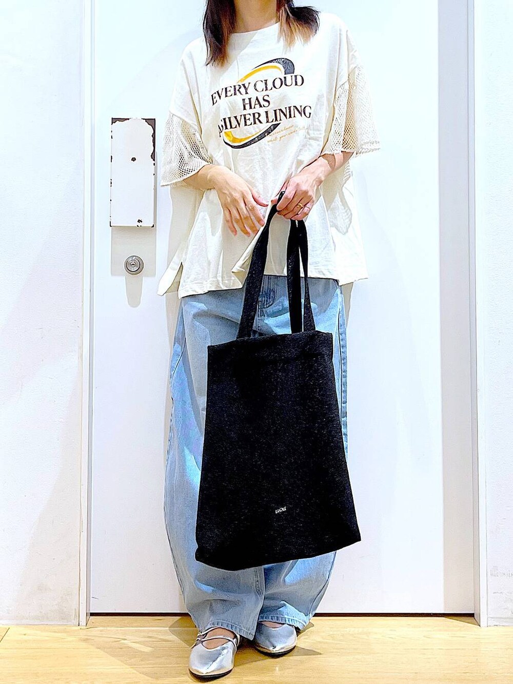 ブラック系のトートバッグ、ブルー系のデニムパンツ、シルバー系のパンプスを着用したレディースの夏コーディネートの6枚目の写真