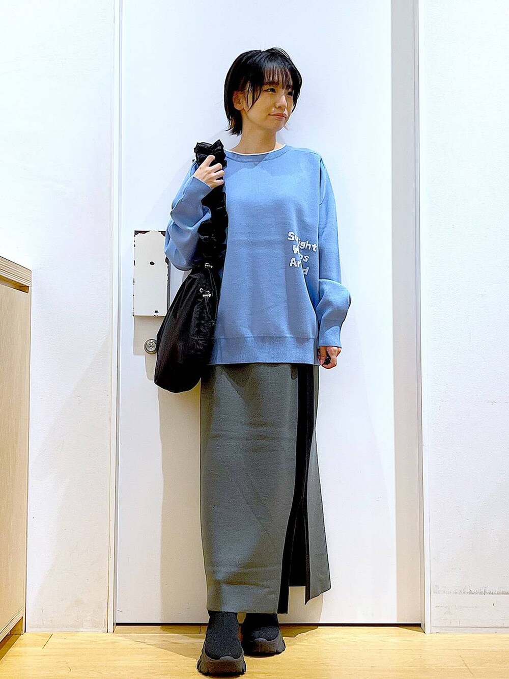 ブルー系のニット/セーター、ブラック系のショルダーバッグ、グレー系のスカートを着用したレディースの冬コーディネートの2枚目の写真