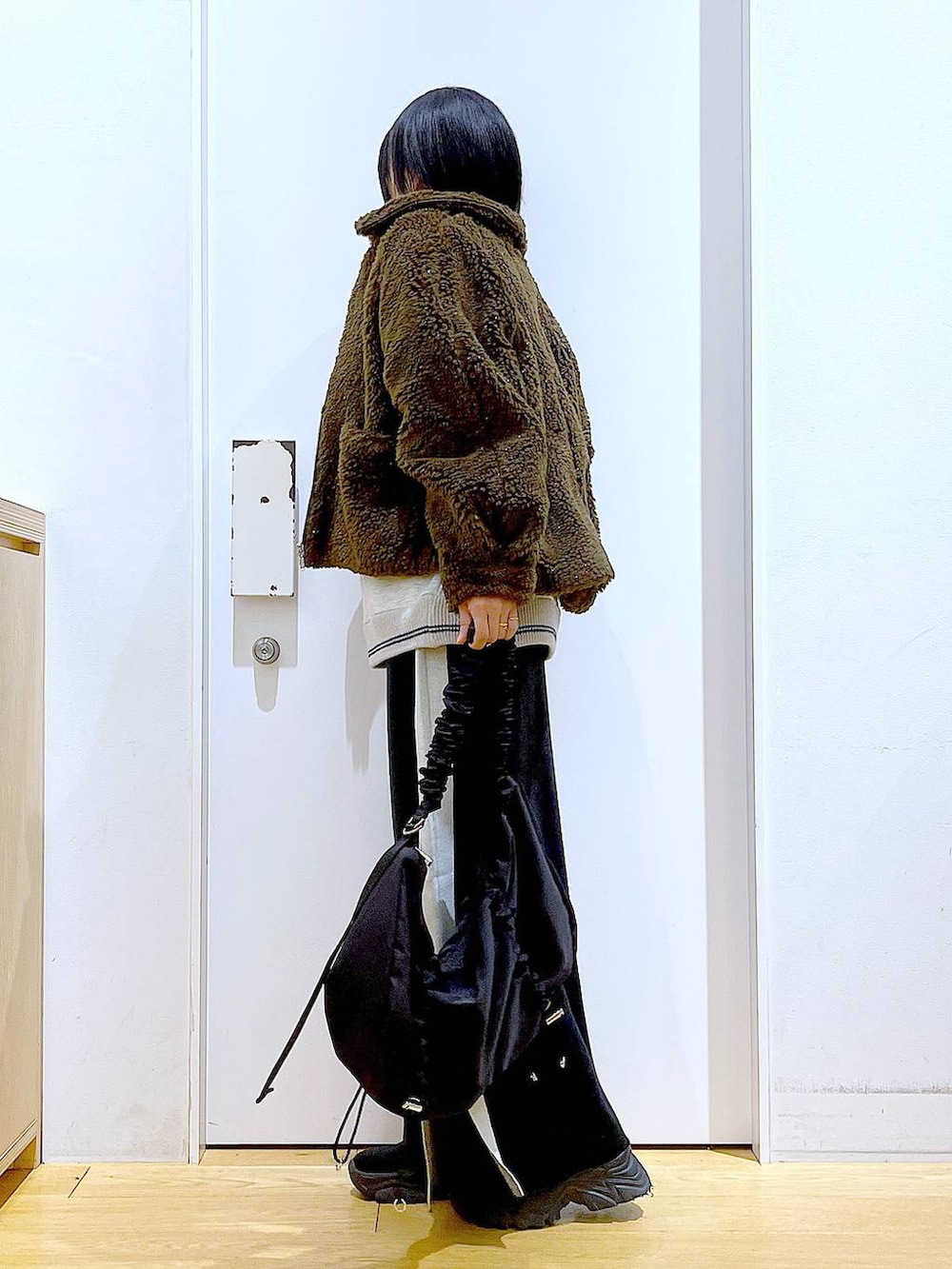 ブラック系のスカート、ブラック系のショルダーバッグ、ブラック系のブーツを着用したレディースの冬コーディネートの3枚目の写真