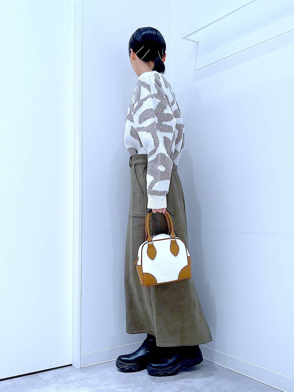 ブラック系のブーツ、ホワイト系のハンドバッグ、グリーン系のスカートを着用したレディースの秋コーディネートの3枚目の写真