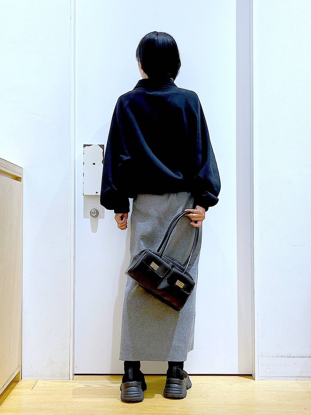 ブラック系のハンドバッグ、ブラック系のブーツ、グレー系のスカートを着用したレディースの冬コーディネートの5枚目の写真