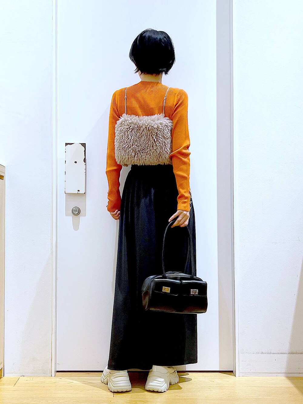 オレンジ系のニット/セーター、ブラウン系のベスト、ブラック系のハンドバッグを着用したレディースの秋コーディネートの5枚目の写真