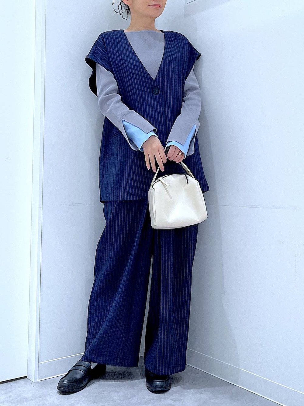 ホワイト系のショルダーバッグ、ブルー系のスラックス、ブルー系のベストを着用したレディースの冬コーディネートの6枚目の写真