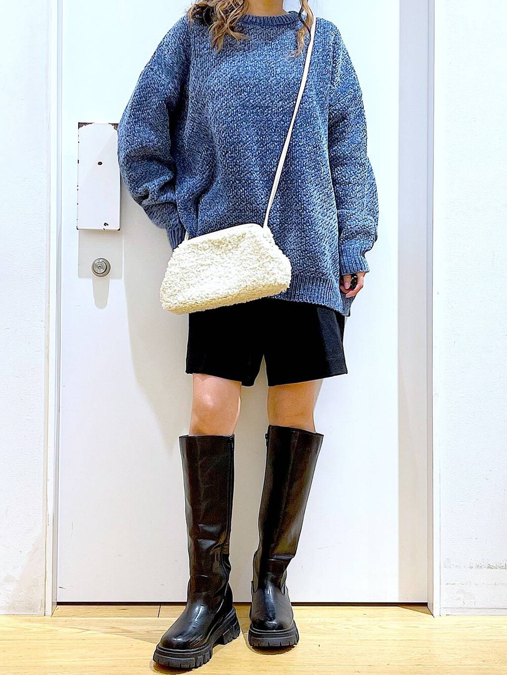 ブルー系のニット/セーター、ホワイト系のクラッチバッグ、ブラック系のブーツを着用したレディースの冬コーディネートの6枚目の写真