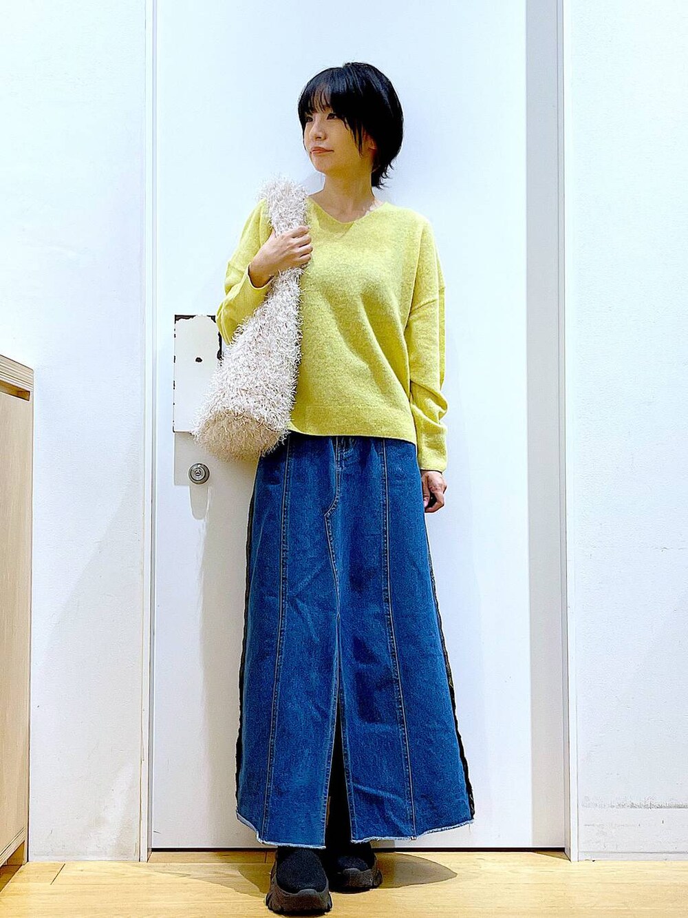 イエロー系のニット/セーター、ブルー系のデニムスカート、ベージュ系のショルダーバッグを着用したレディースの冬コーディネートの2枚目の写真