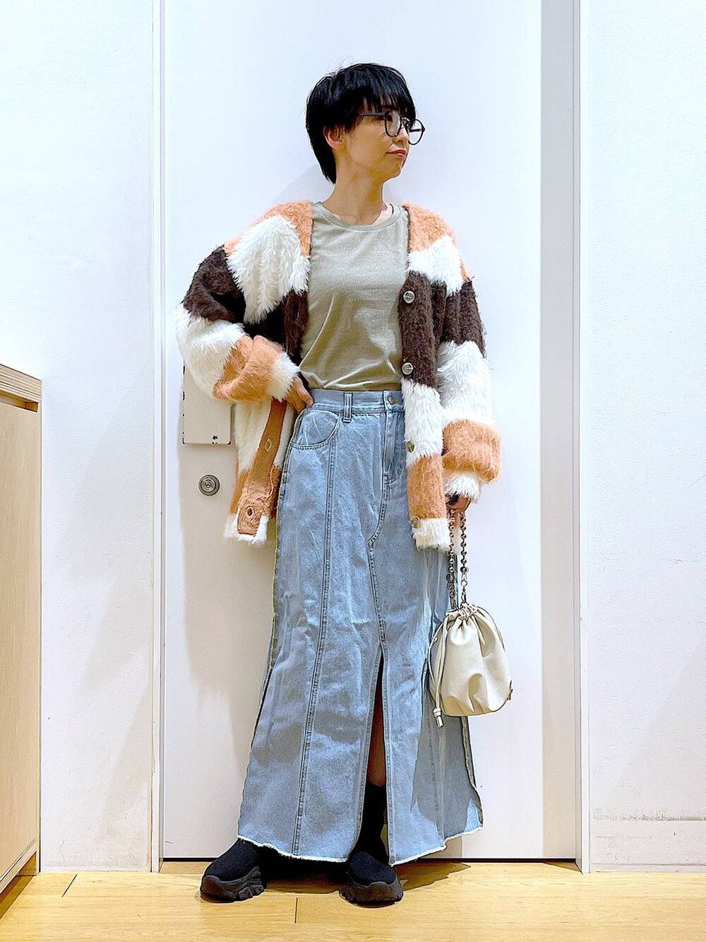 ベージュ系のショルダーバッグ、ブルー系のデニムスカート、ブラック系のブーツを着用したレディースの冬コーディネートの2枚目の写真