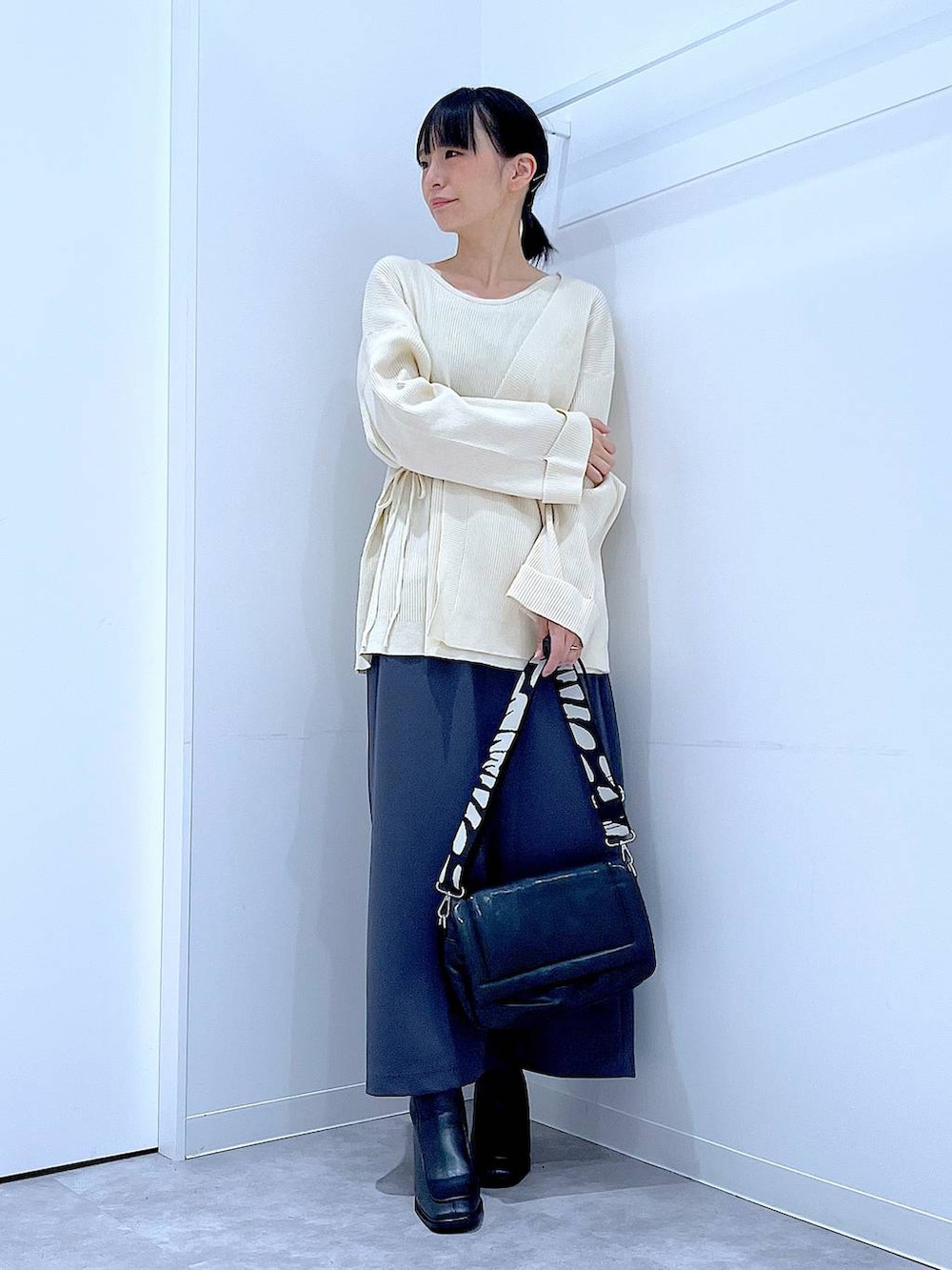 グレー系のスカート、ブラック系のショルダーバッグ、ブラック系のブーツを着用したレディースの冬コーディネートの2枚目の写真