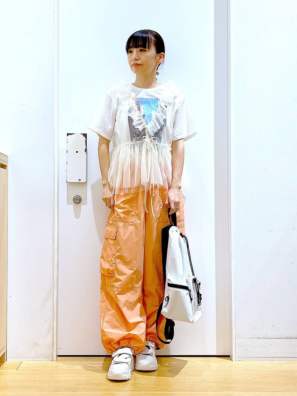 ホワイト系のスニーカー、ホワイト系のショルダーバッグ、オレンジ系のカーゴパンツを着用したレディースの夏コーディネートの2枚目の写真