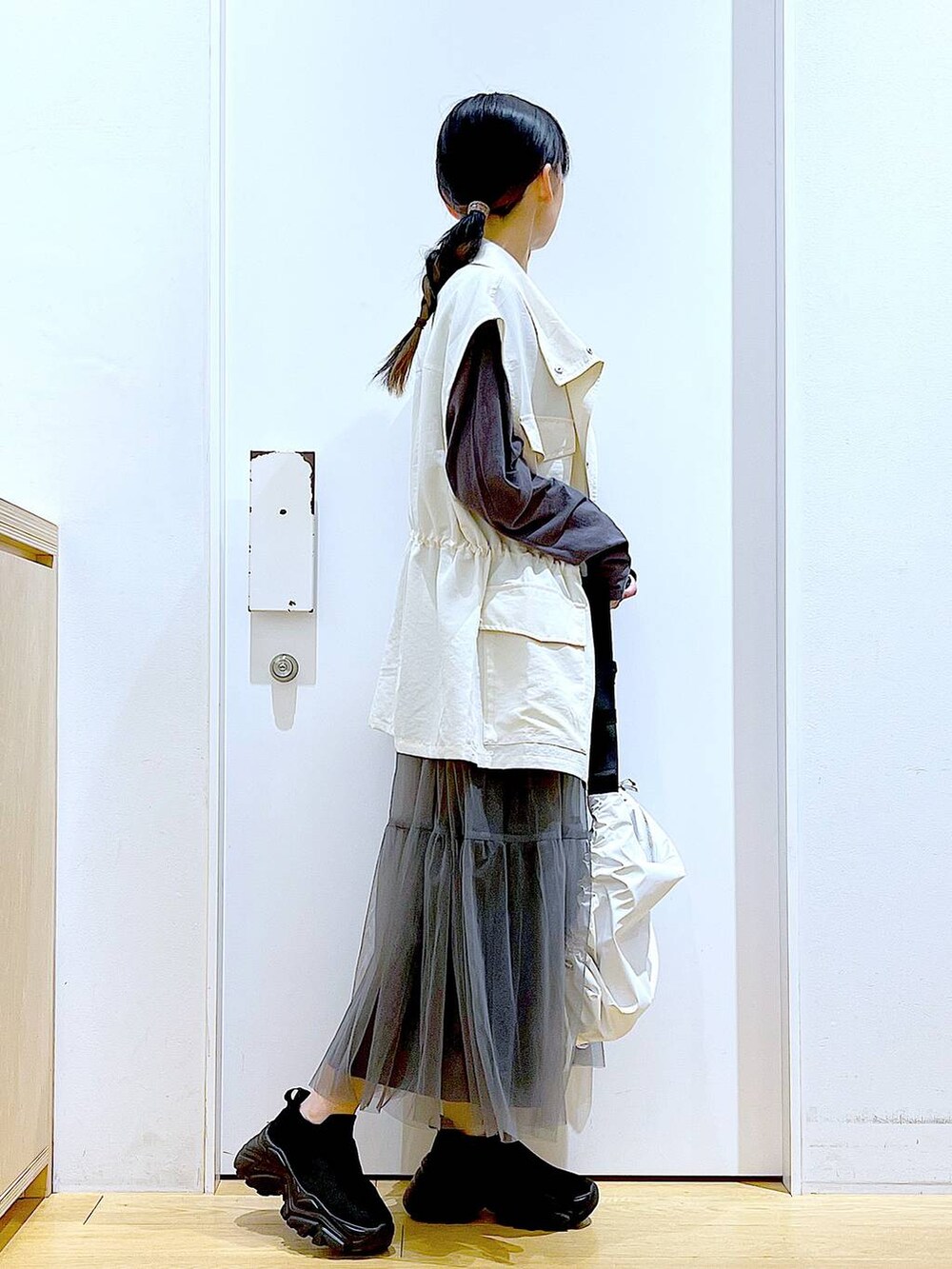 グレー系のスカート、ブラック系のスニーカー、ホワイト系のベストを着用したレディースの春コーディネートの4枚目の写真