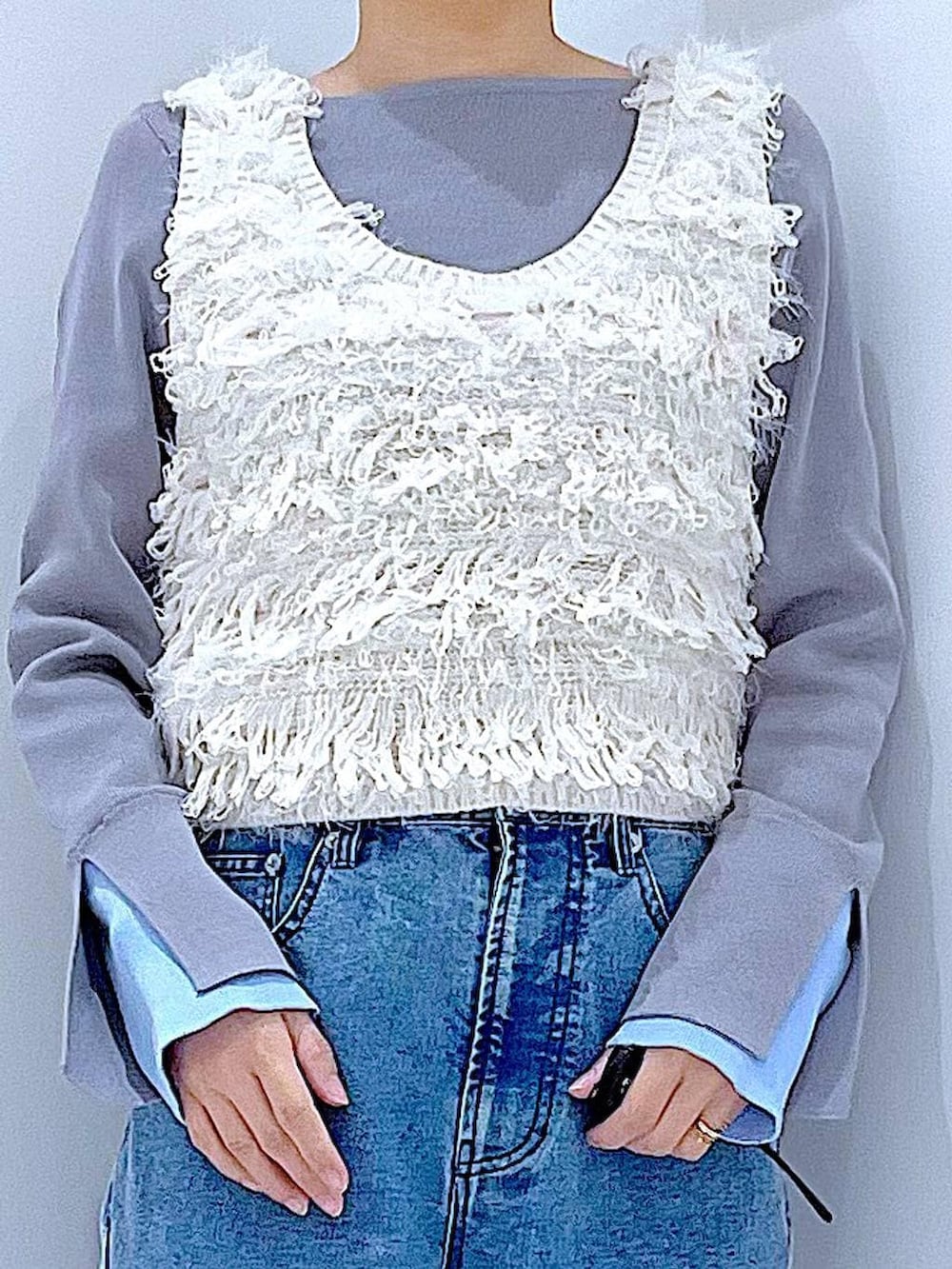 ホワイト系のベスト、グレー系のニット/セーター、ブルー系のデニムパンツを着用したレディースの春コーディネートの7枚目の写真