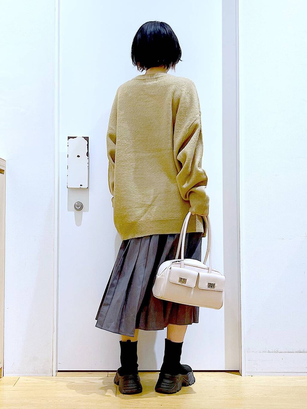 ホワイト系のハンドバッグ、ブラック系のブーツ、グレー系のスカートを着用したレディースの冬コーディネートの5枚目の写真