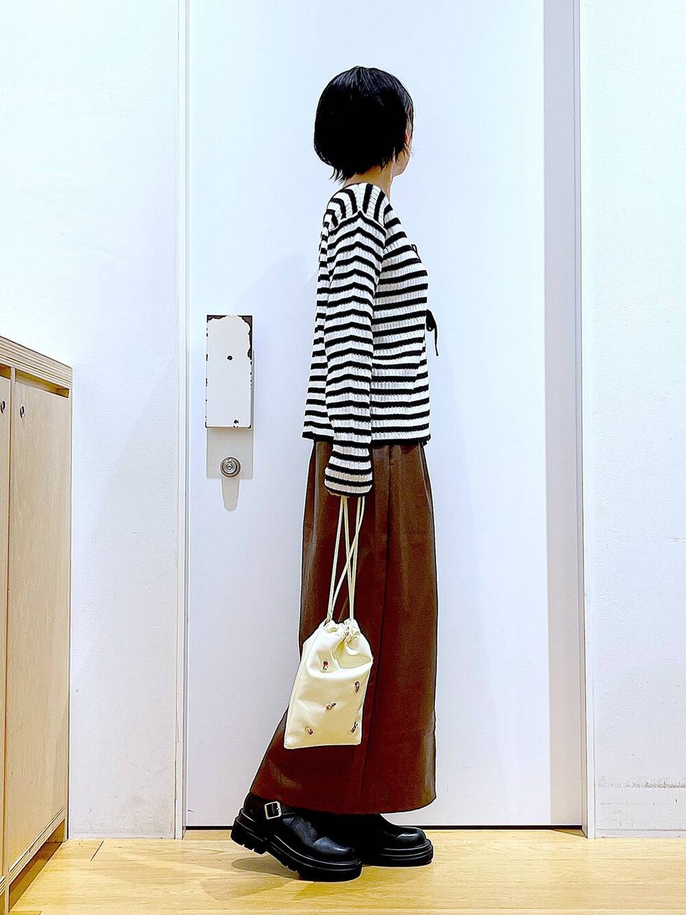 ブラウン系のスカート、ホワイト系のショルダーバッグ、ブラック系のブーツを着用したレディースの秋コーディネートの4枚目の写真
