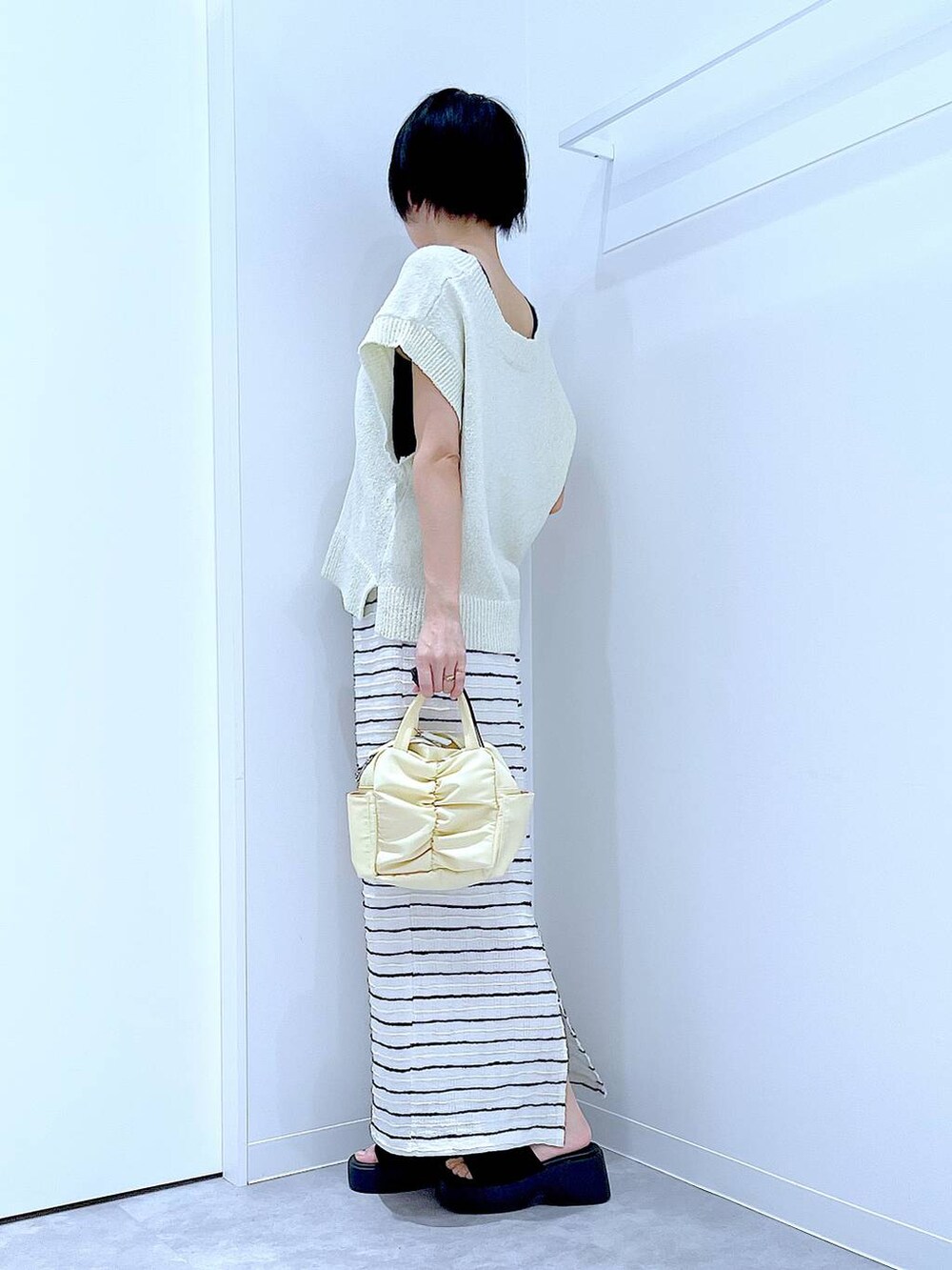 ブラック系のサンダル、イエロー系のショルダーバッグ、ホワイト系のスカートを着用したレディースの夏コーディネートの3枚目の写真