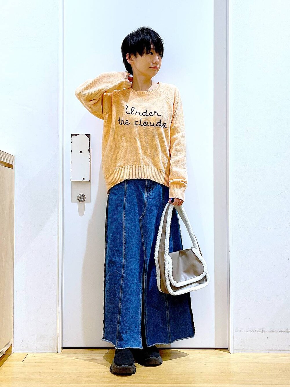 ブルー系のデニムスカート、ベージュ系のショルダーバッグ、ブラック系のブーツを着用したレディースの冬コーディネートの2枚目の写真