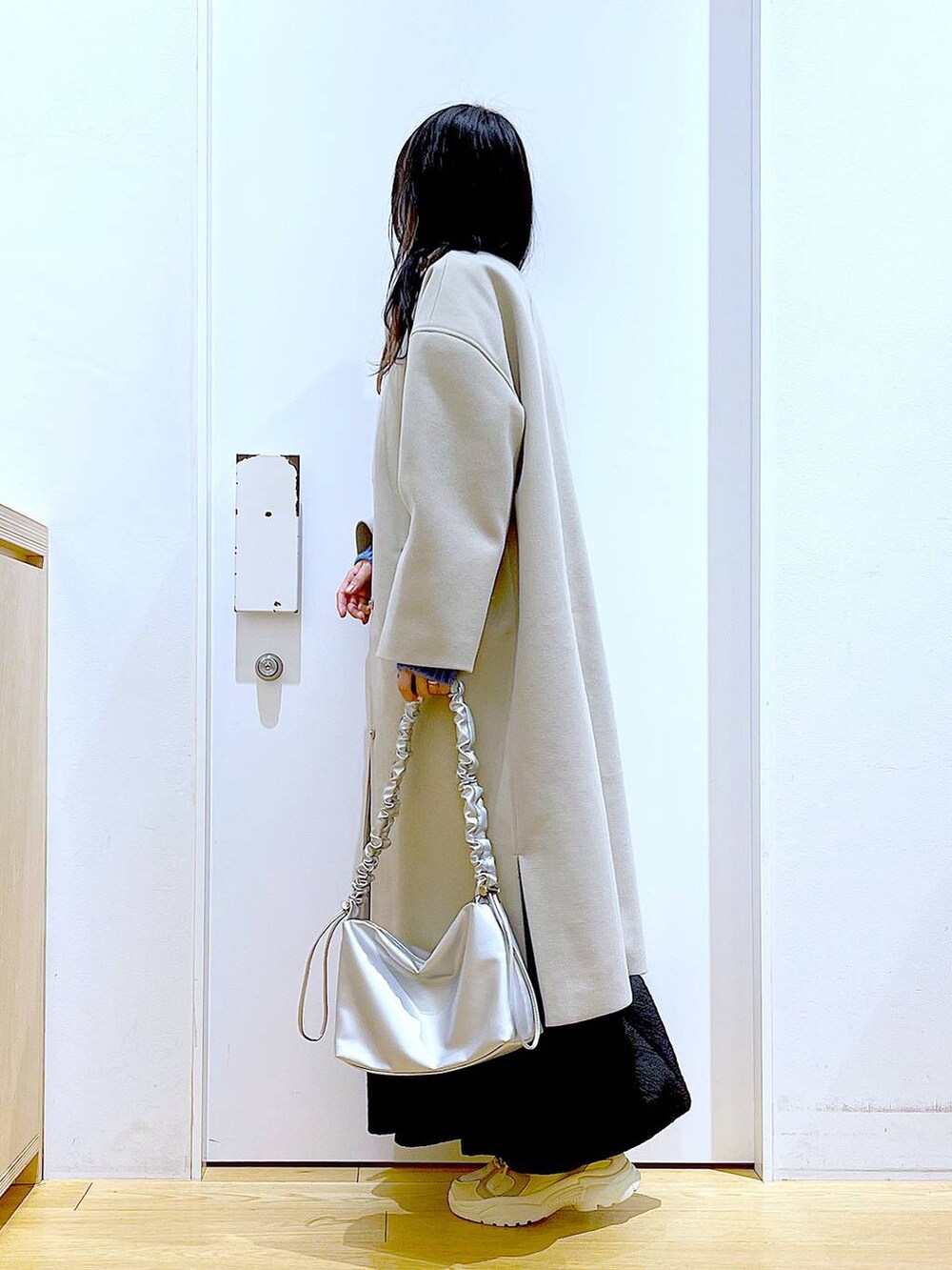 シルバー系のショルダーバッグ、ベージュ系のスニーカー、ベージュ系のノーカラーコートを着用したレディースの冬コーディネートの3枚目の写真