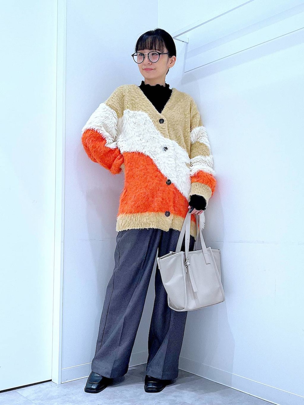 オレンジ系のカーディガン/ボレロ、ブラック系のブーツ、グレー系のスラックスを着用したレディースの冬コーディネートの2枚目の写真