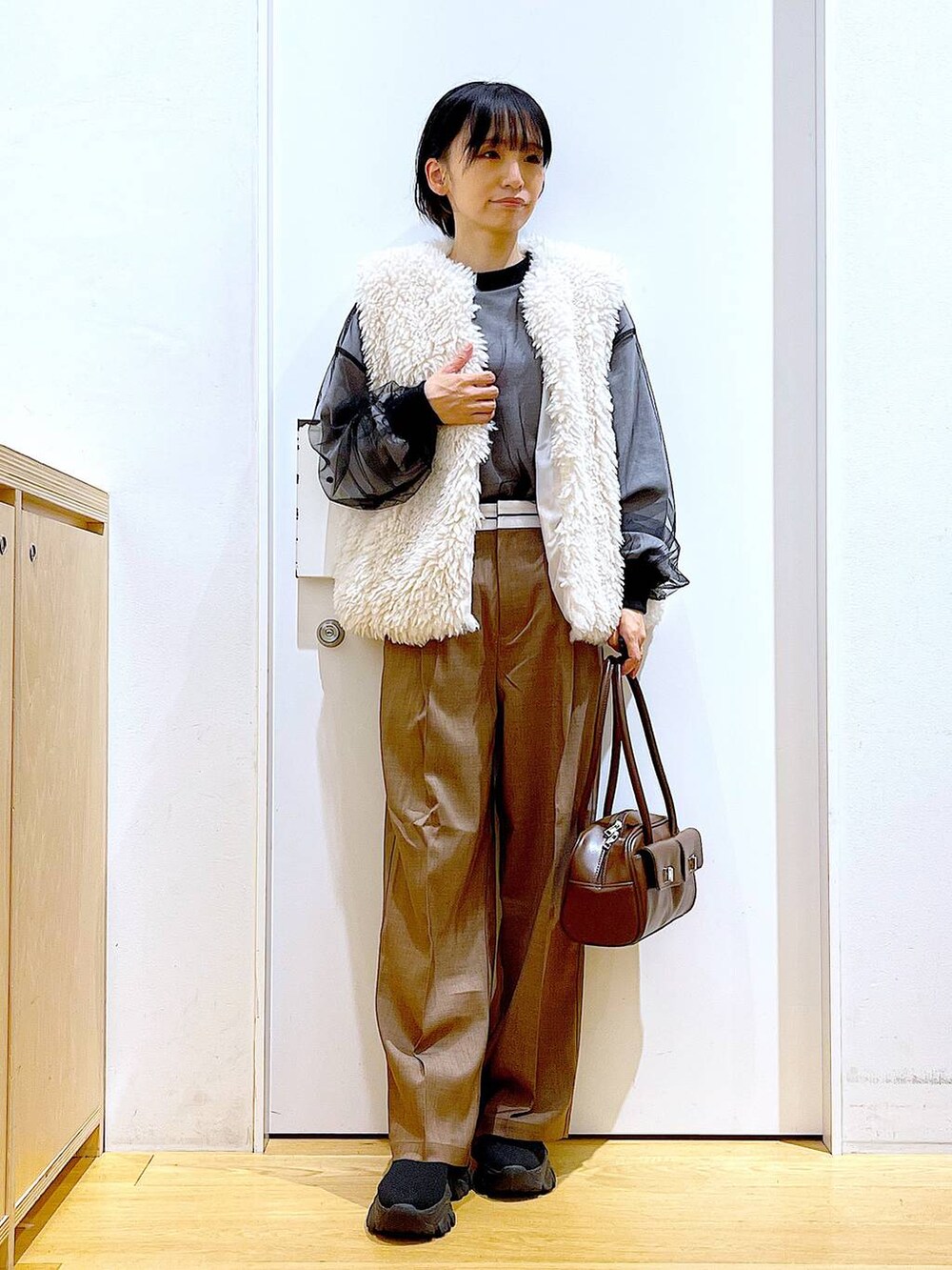 ベージュ系のベスト、ブラウン系のハンドバッグ、ブラック系のブーツを着用したレディースの冬コーディネートの2枚目の写真