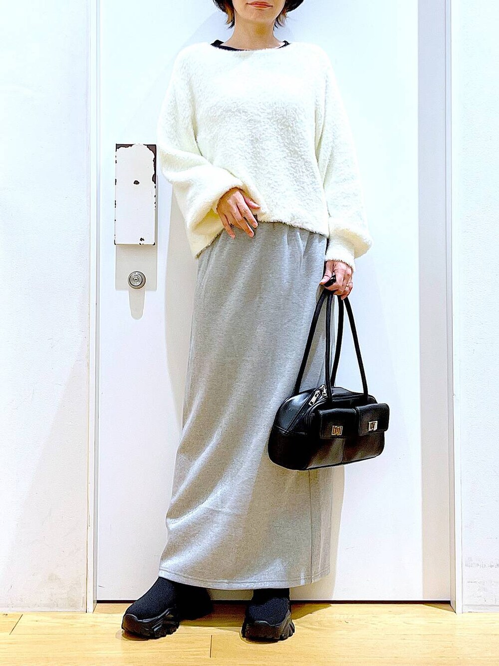 ブラック系のハンドバッグ、ブラック系のブーツ、グレー系のスカートを着用したレディースの冬コーディネートの6枚目の写真